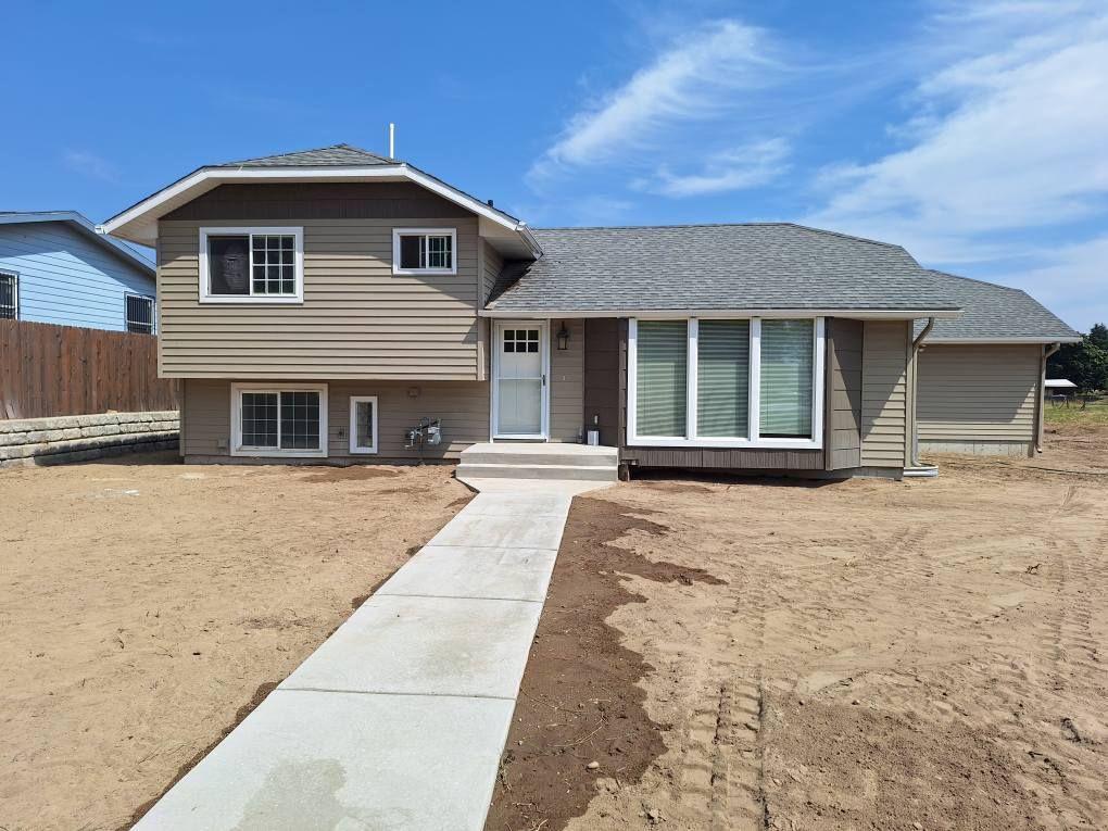 A light brown bi-level house with a gray roof and a new concrete walkway set against a clear blue sky.