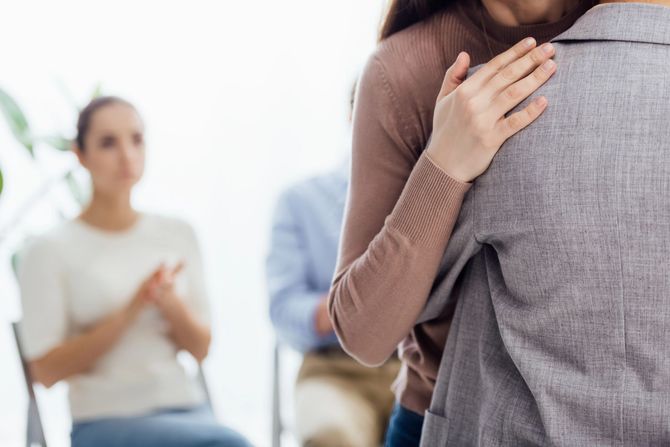 Due persone che si abbracciano durante una seduta di terapia, con una persona sfocata seduta sullo sfondo.