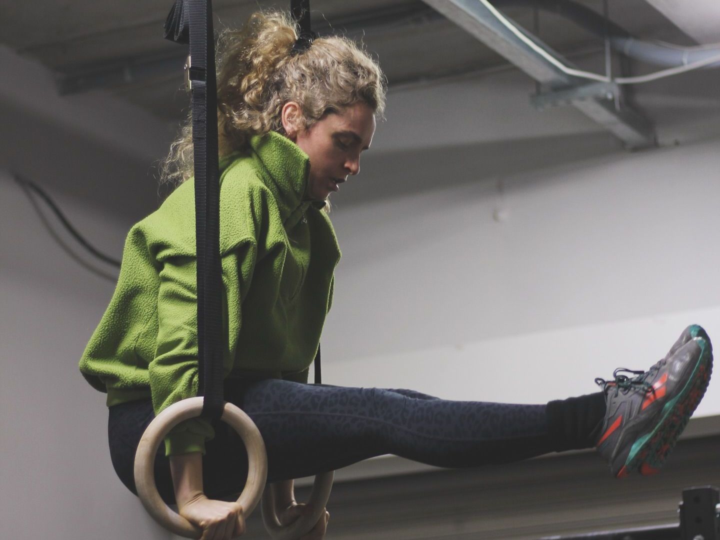 A woman in a green jacket is doing exercises on gymnastic rings