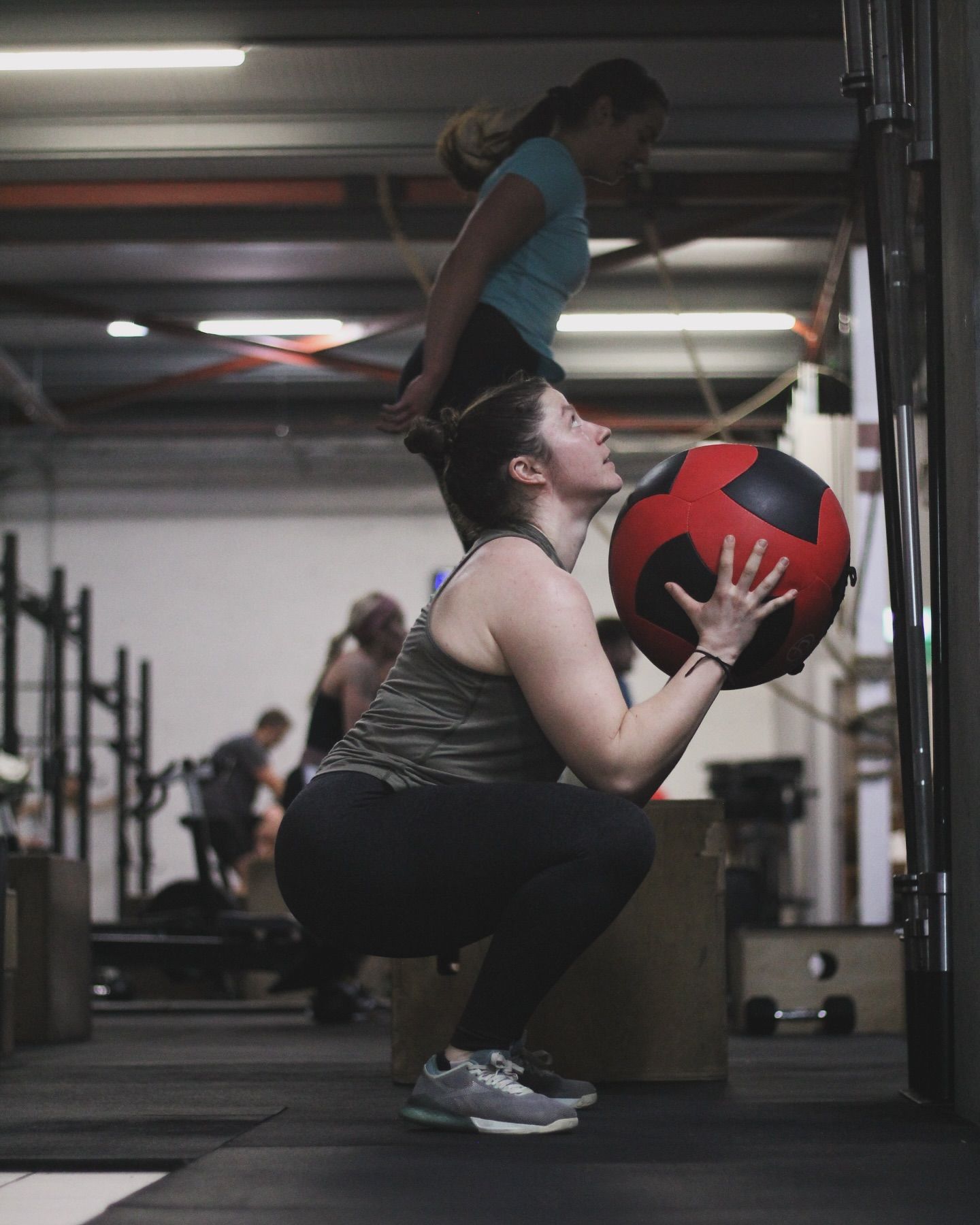 A woman is squatting down while holding a medicine ball in a gym.