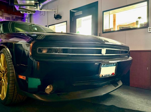 Black sports car parked in a garage with bright windows and workshop tools nearby | Exodus Motor Works LLC