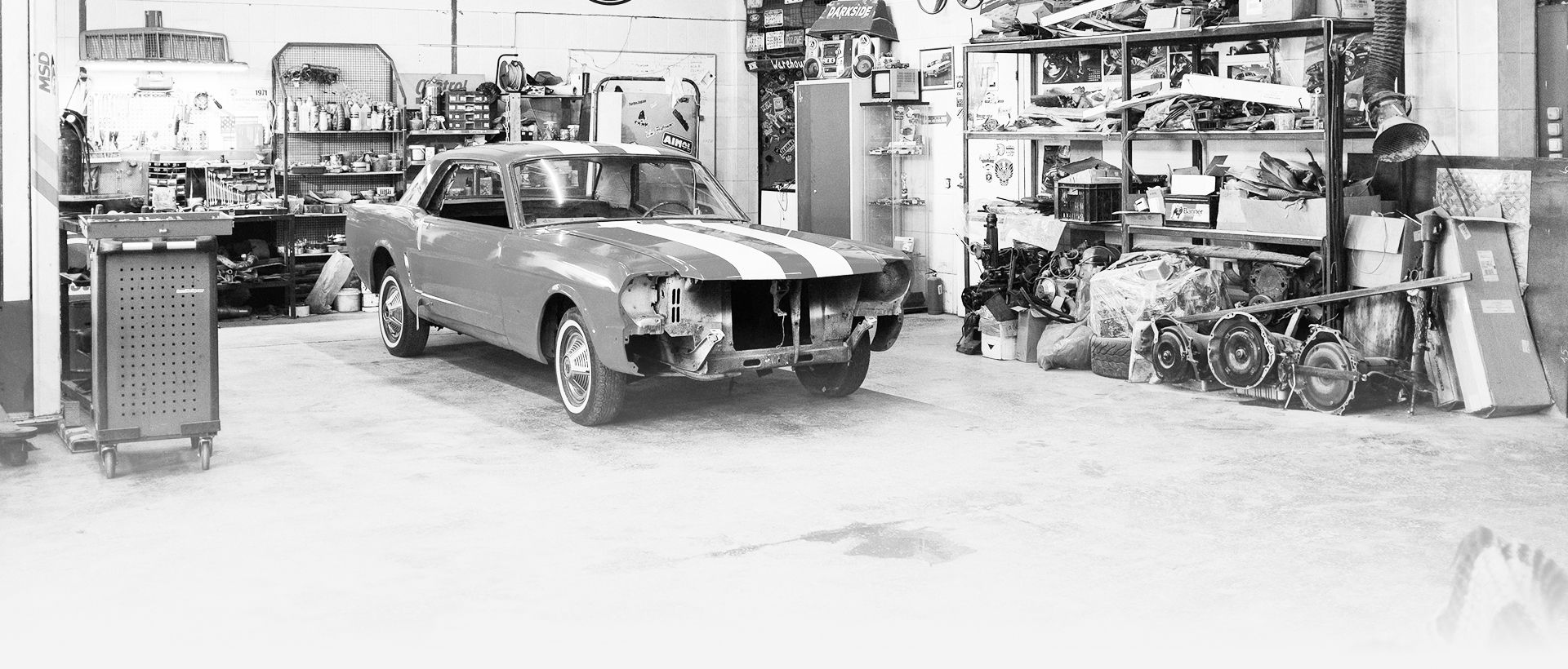 Vintage car in a garage workshop, surrounded by tools, equipment, and shelves of parts. | Exodus Motor Works LLC