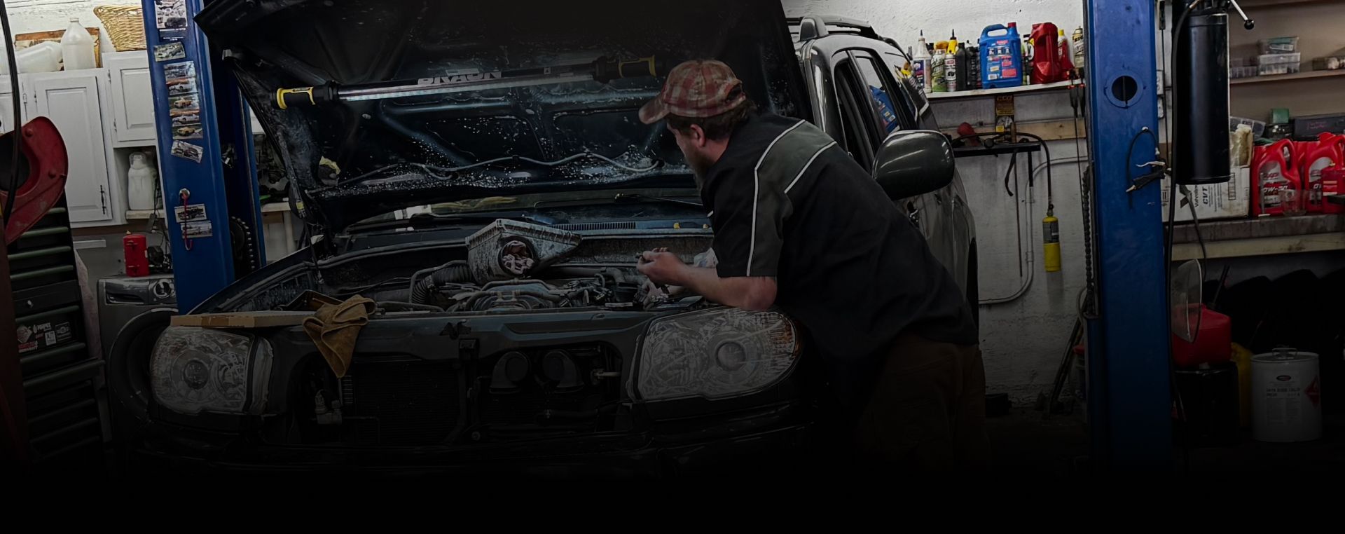 Mechanic working on a car engine in a dim garage, with tools and equipment nearby. | Exodus Motor Works LLC