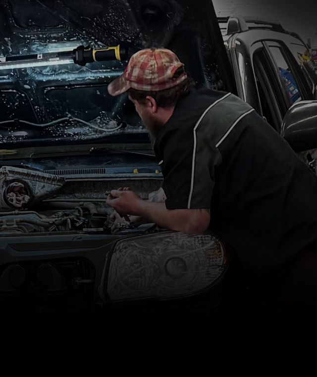 Mechanic working under a car hood in a garage, with tools and engine parts visible | Exodus Motor Works LLC