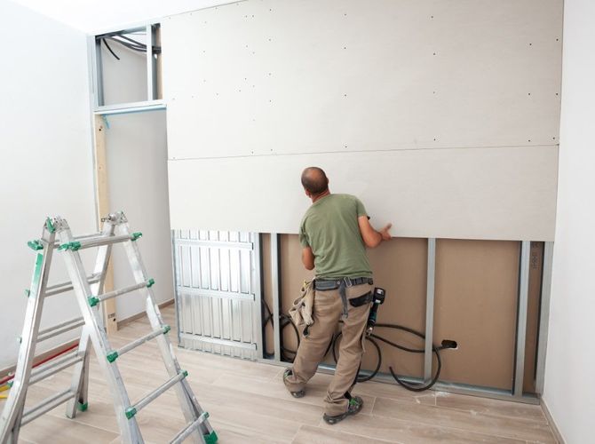 Worker installing a large white wall panel in a room under renovation