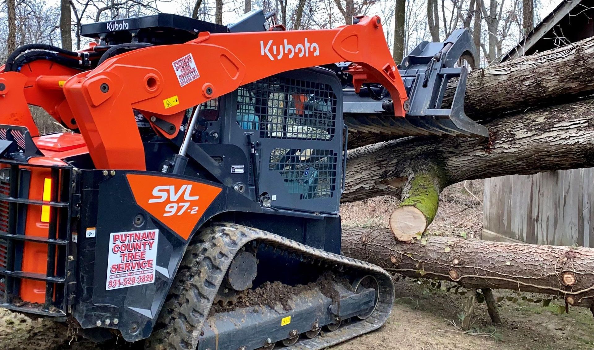Orange Kubota SVL97-2 skid steer lifting a cut tree trunk in an outdoor setting.