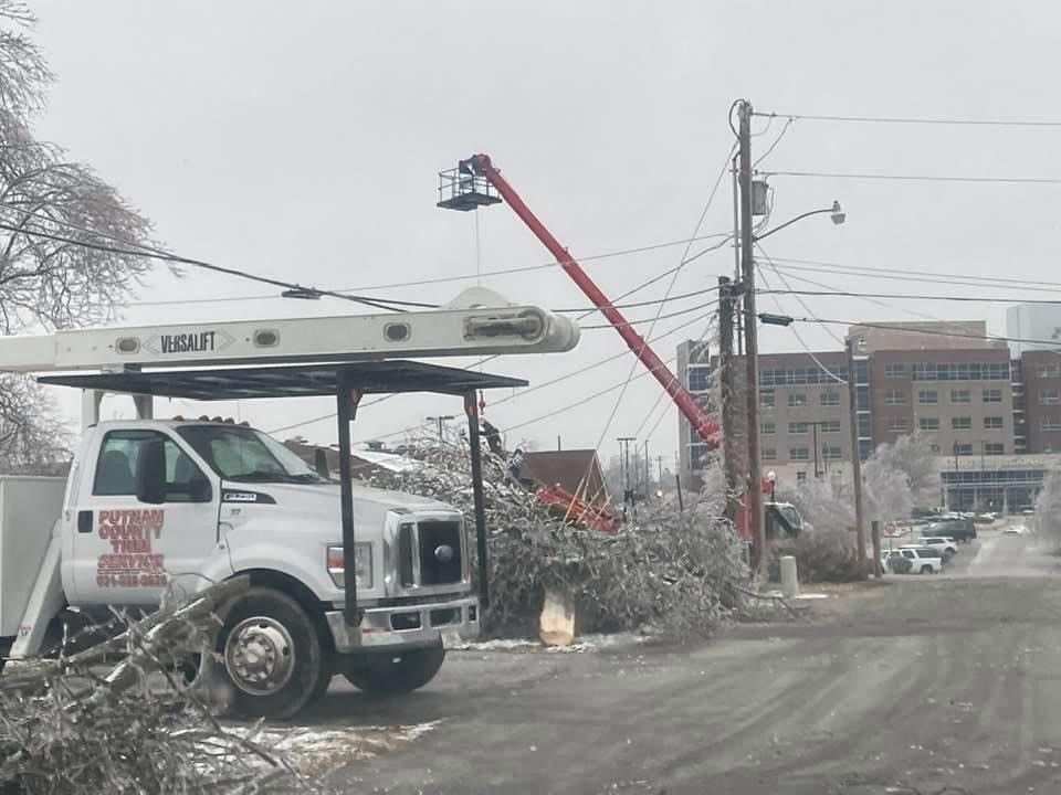Skid Steer Loader Used For Earth Moving Landscaping — Cookeville, TN — Putnam County Tree Service White utility truck and lift repairing power lines; ice-covered trees and a building in the background.