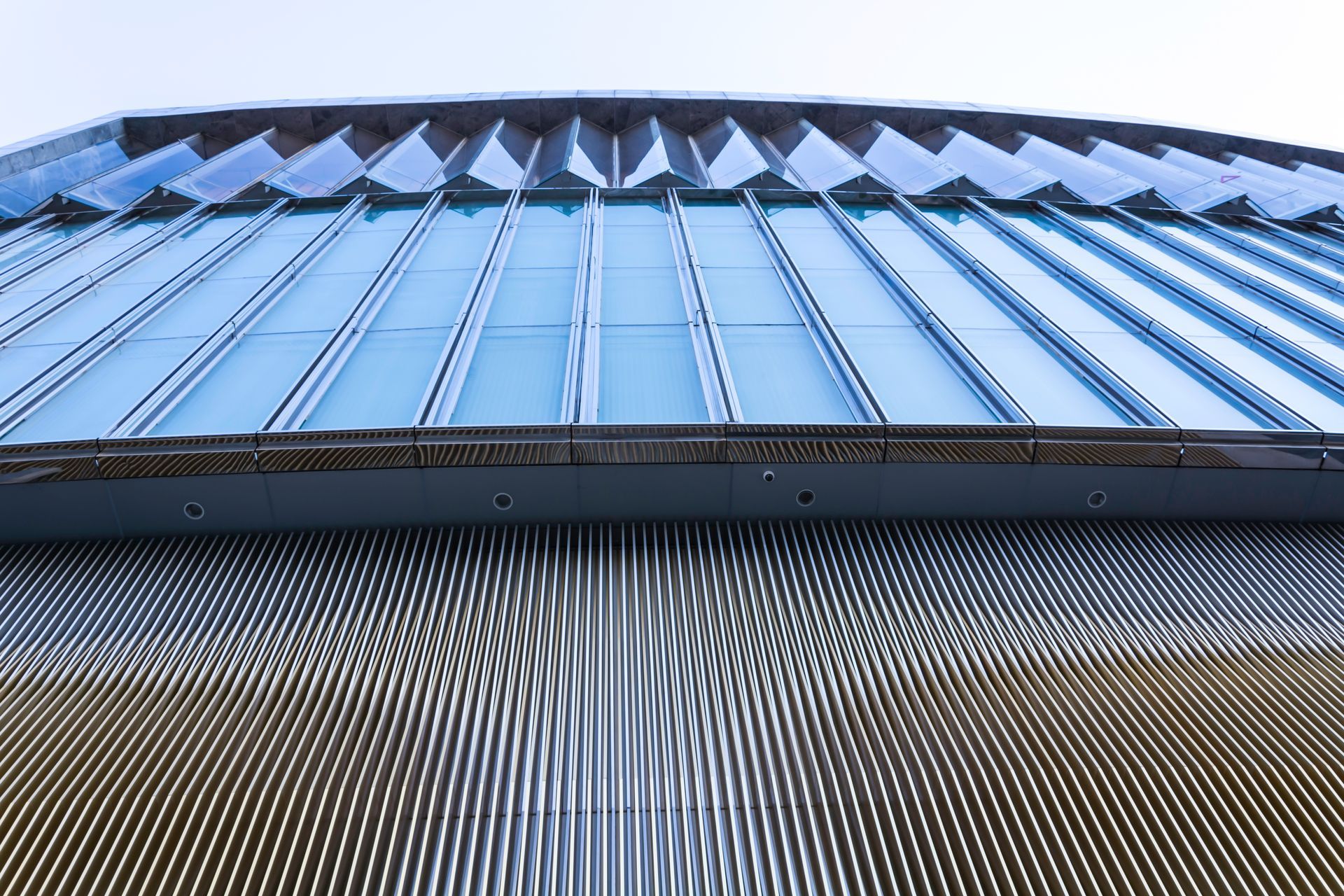 Low-angle view of a blue metal building facade with a curved roofline and patterned lower wall