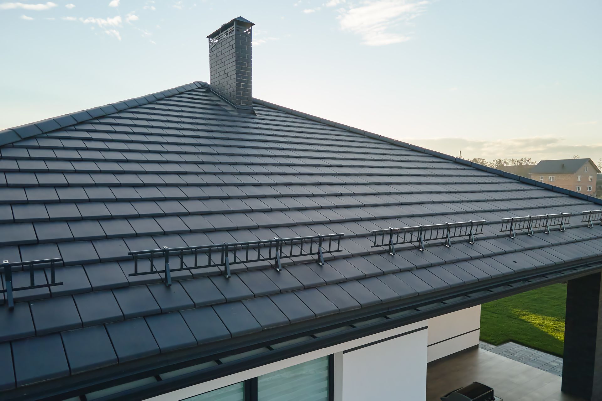 Modern house roof with dark gray tiles and a chimney under a clear sky
