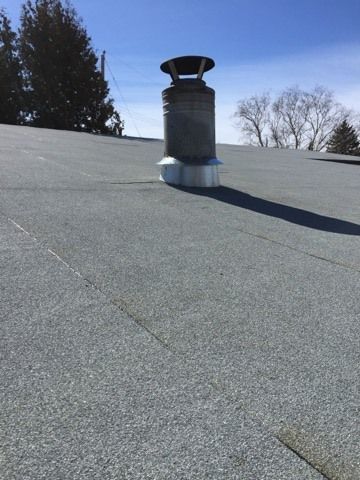 A chimney on top of a roof with trees in the background.