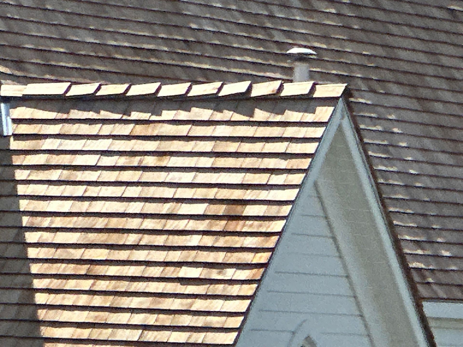 Close-up of a house roof with brown shingles and a light gray dormer window.
