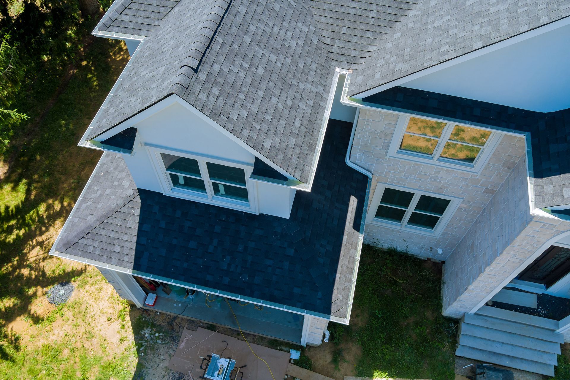 Aerial view of a gray house with a dark roof and white trim, surrounded by trees and a small yard