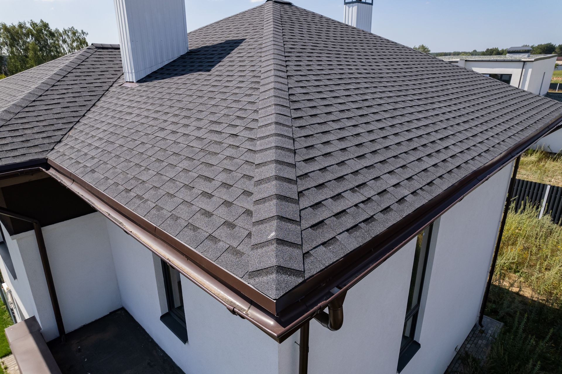 Dark gray shingled roof on a white house with brown gutters and two white chimneys.