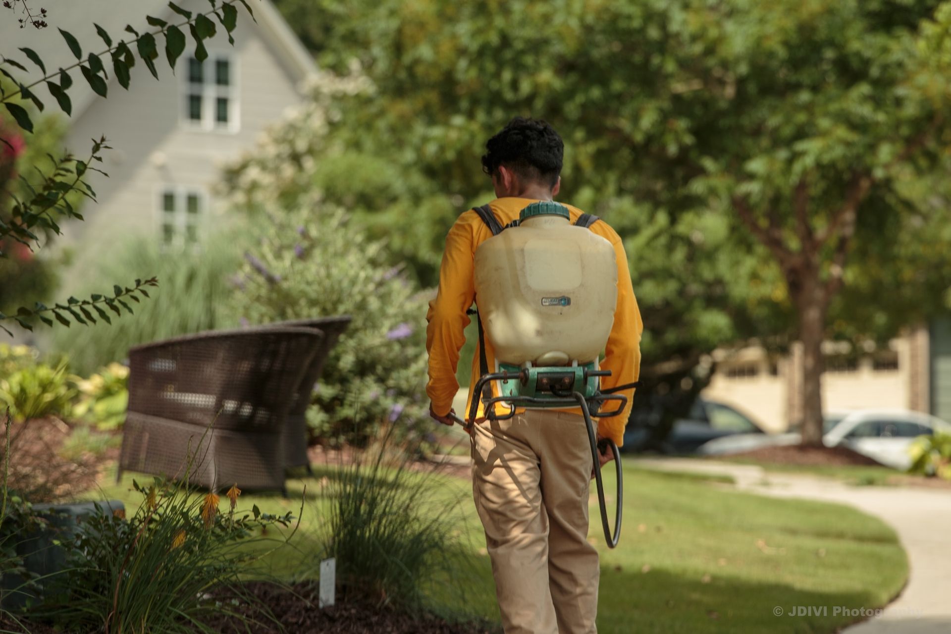 Man in yellow shirt sprays lawn with backpack sprayer.
