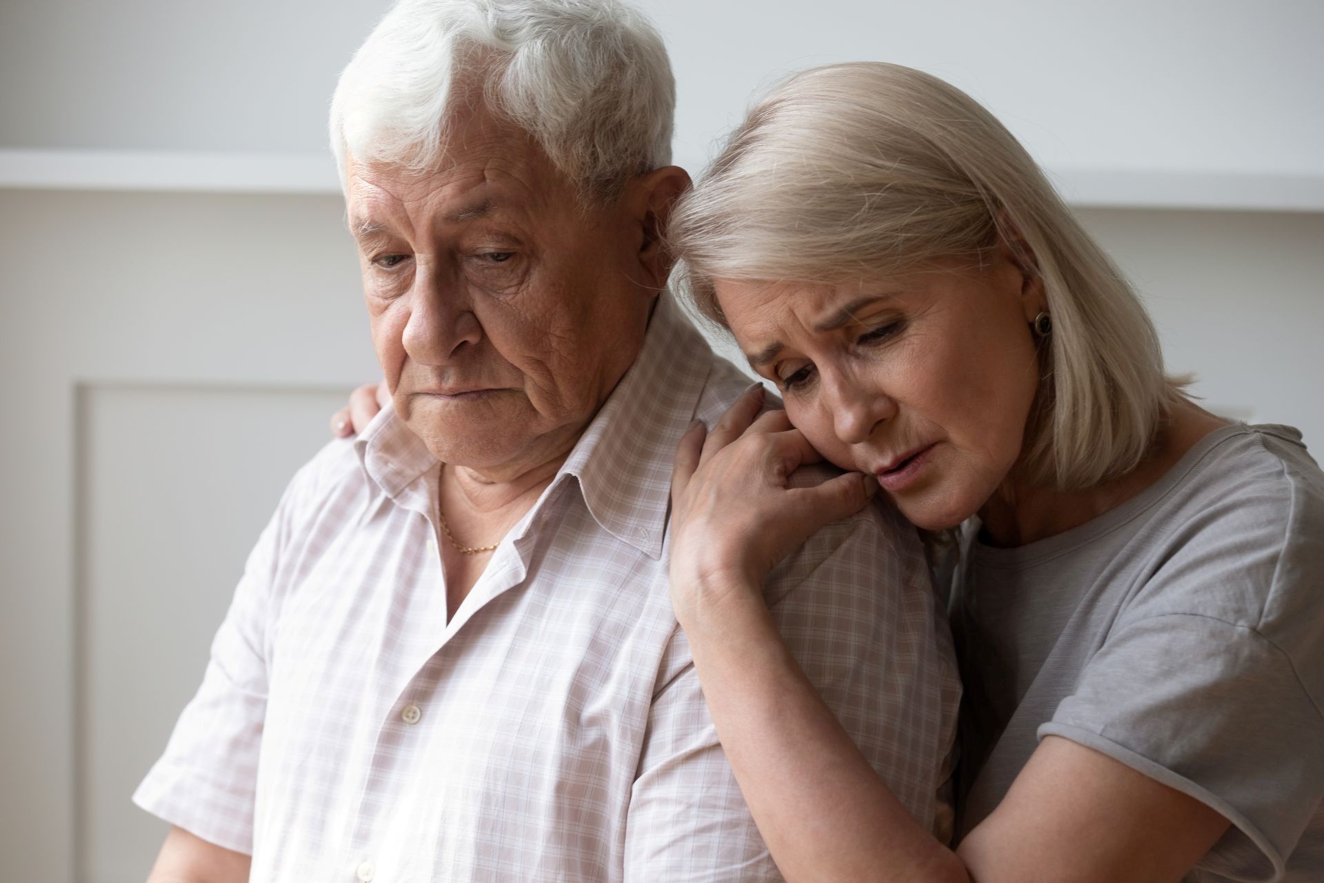 Woman comforts an elderly person, both looking somber. The woman has her arm around the man's shoulders.