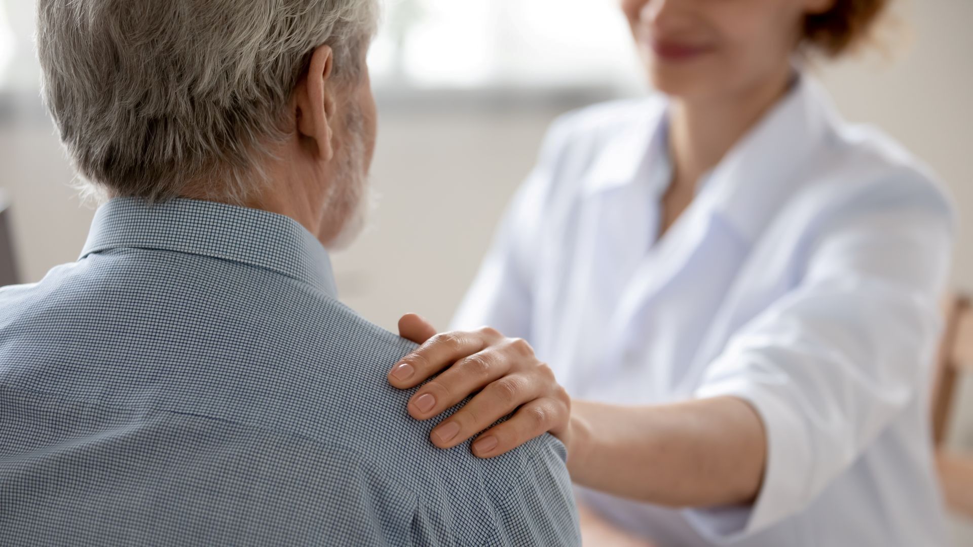 Medical professional comforts a patient, hand on shoulder.