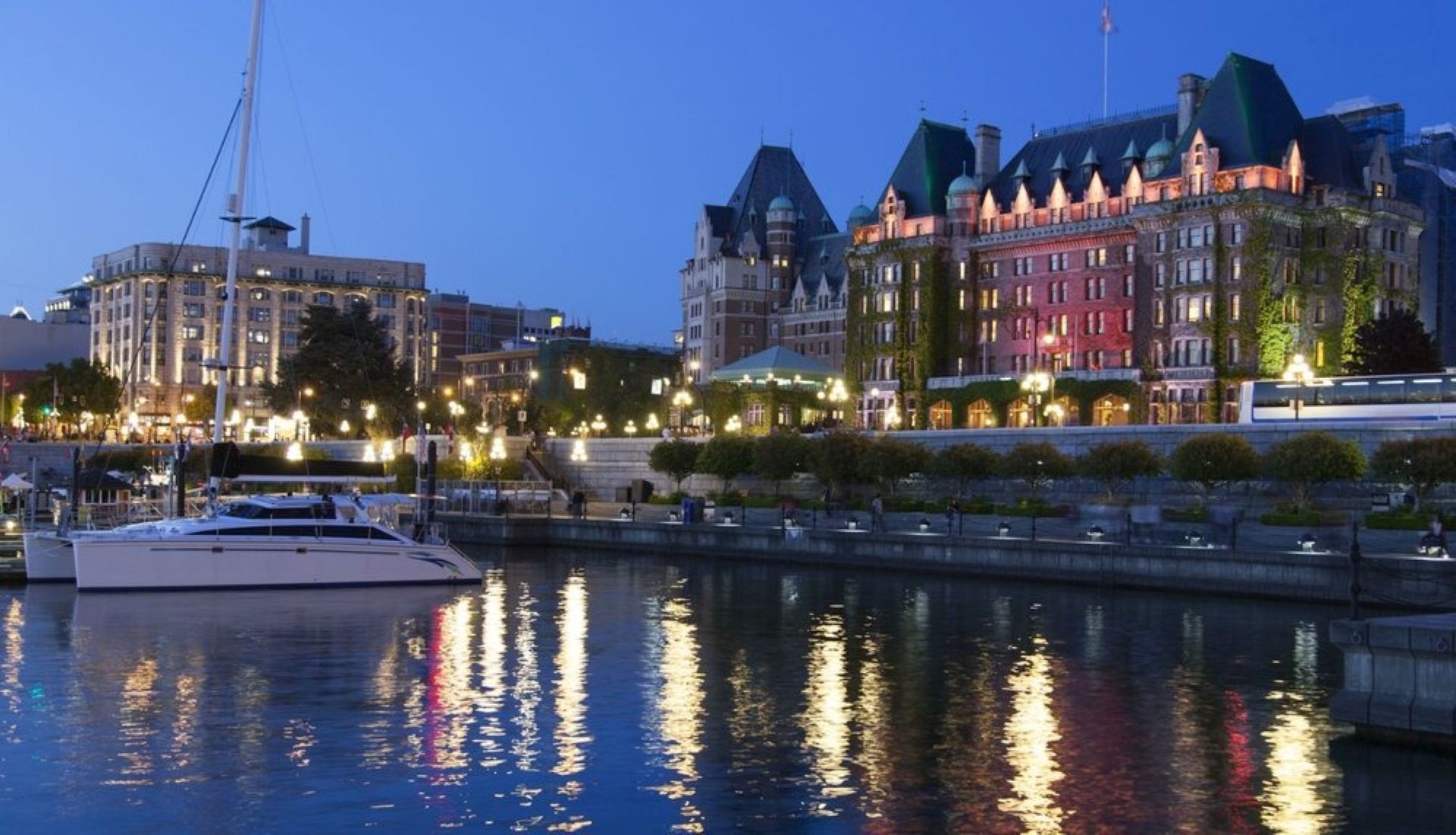 Waterfront at dusk with illuminated buildings and reflections in the water; boat in foreground.