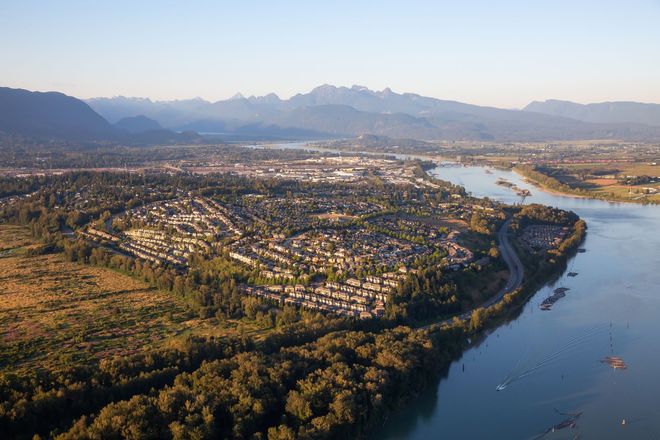 Aerial view of a city bordering a river, with mountains in the background under a clear sky.