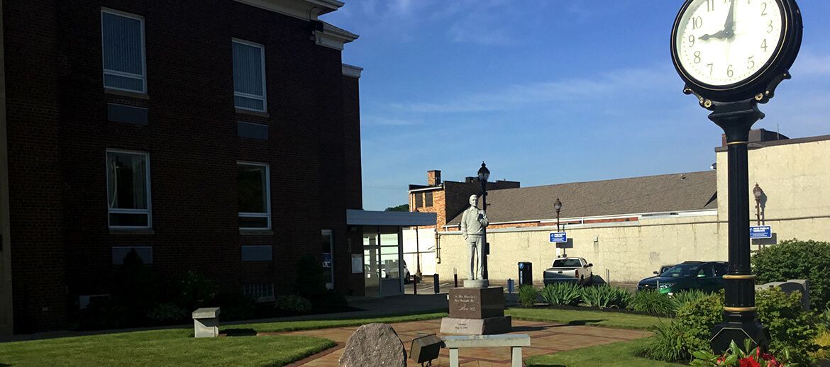 a clock tower with a statue in front of a building .