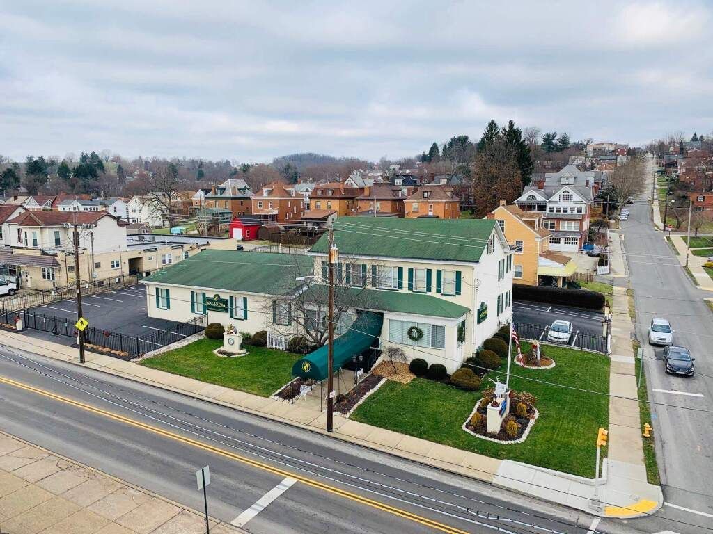 an aerial view of a large white house with a green roof next to a street .