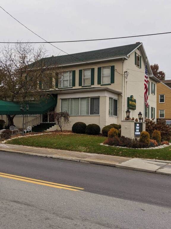a large white house with green shutters is on the side of the road