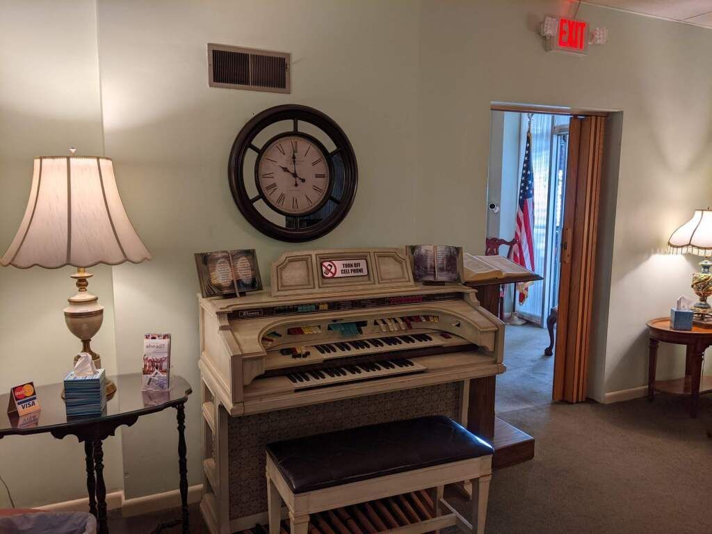 there is a clock on the wall above the organ in the room .