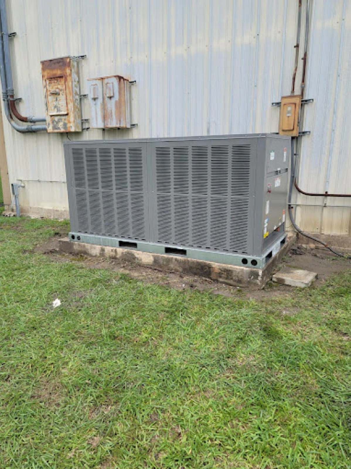 A large air conditioner is sitting in the grass in front of a building.
