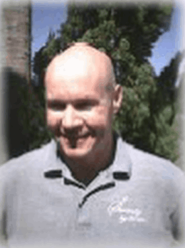 A bald man wearing a grey shirt is smiling for the camera