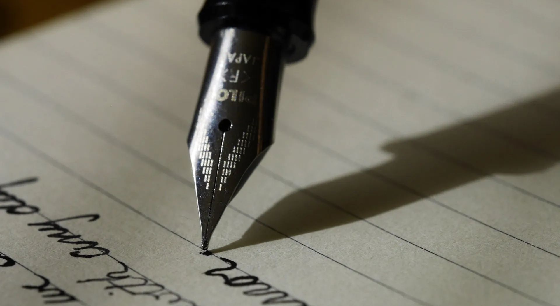 A black fountain pen writing on lined paper, casting a shadow.