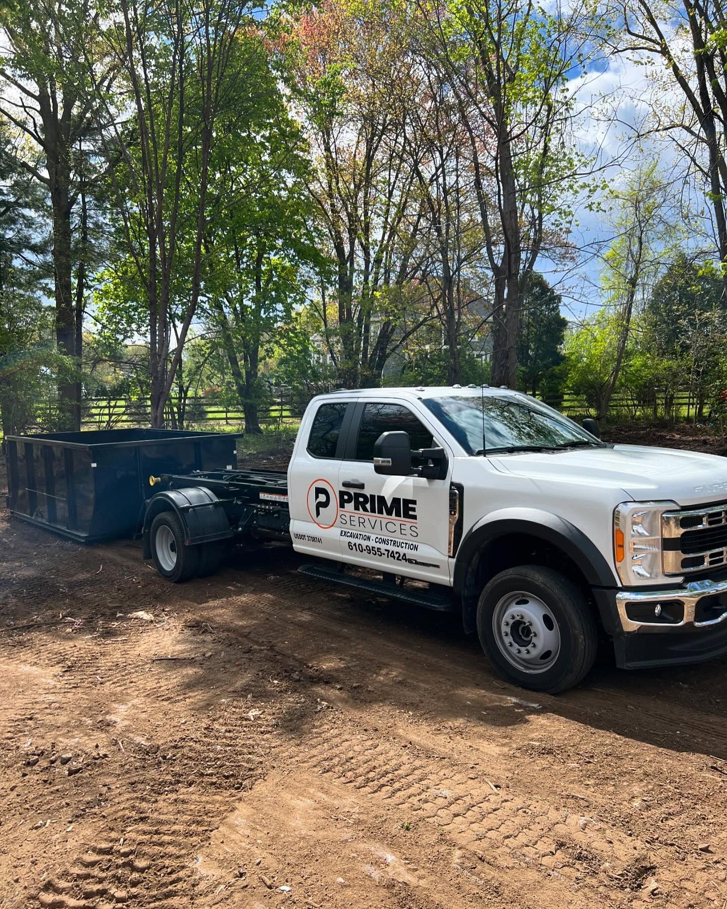 White PRIME truck with a black trailer parked on a dirt road in a wooded area.