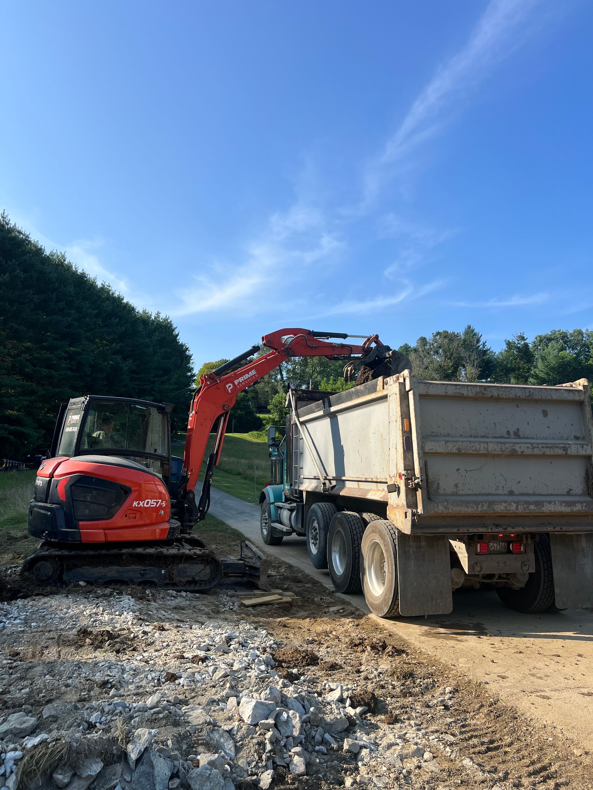 Red excavator loading soil into a dump truck on a muddy construction site under a blue sky