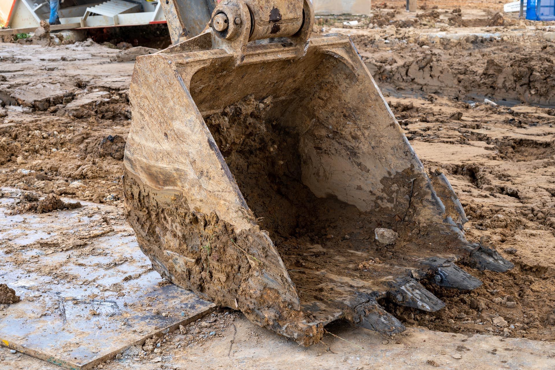 Close-up of a muddy excavator bucket digging into soil at a construction site