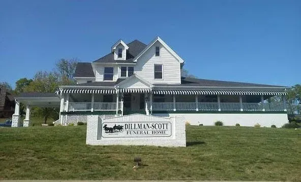 White house with wraparound porch on a grassy hill under a blue sky; sign reads "Oldham's Rest B&B"