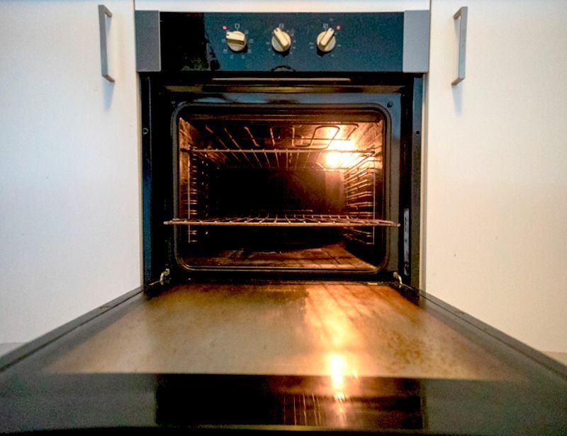 Open oven with glowing interior and empty racks, viewed from the kitchen