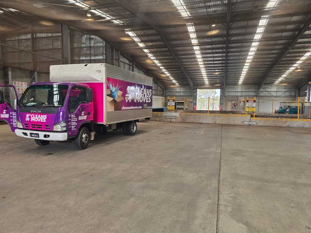 Purple and pink Cleans and Moves Removalist truck parked inside a large waste disposal location.