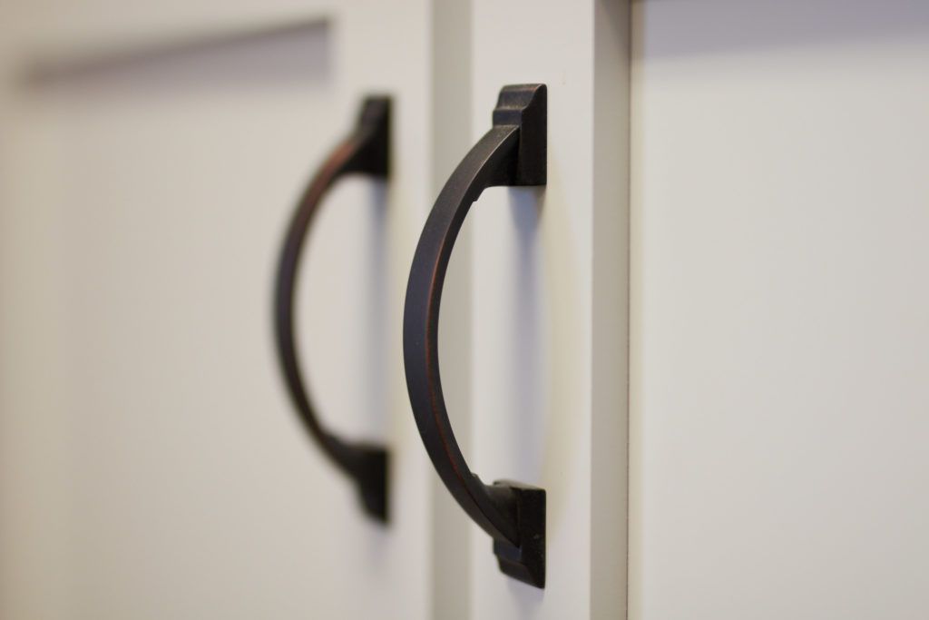 a close up of two black cabinet handles on a white cabinet .