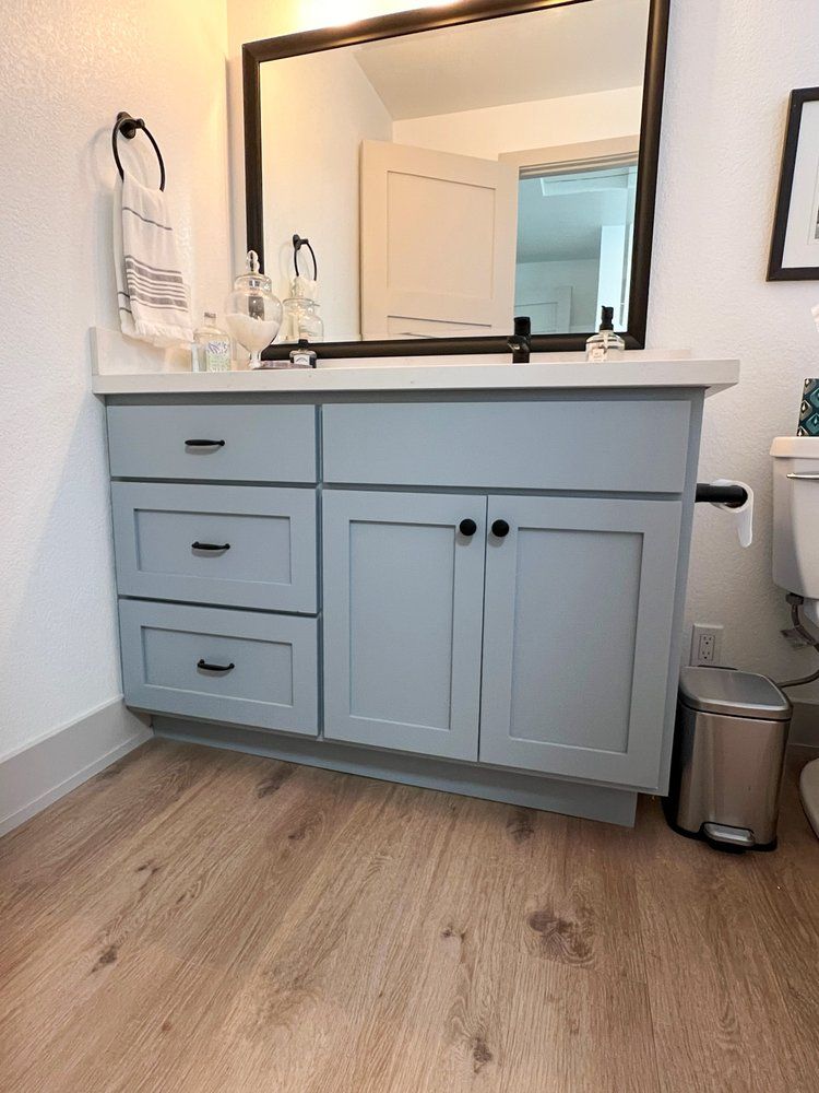 a bathroom vanity with a sink , mirror and trash can .