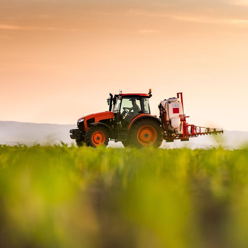 A tractor is spraying a field of grass at sunset.