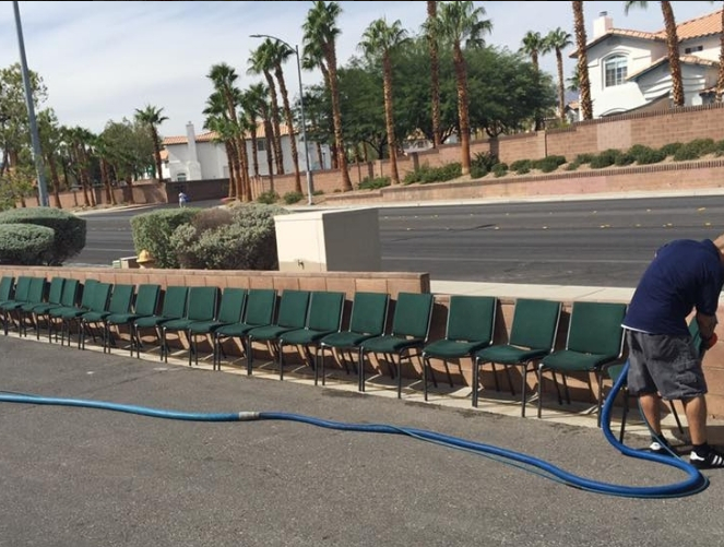 Row of green chairs beside a road, with a worker handling a blue hose in the foreground.