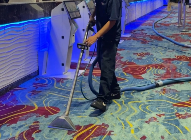 Person using a metal detector on a patterned carpet in a blue-lit hallway