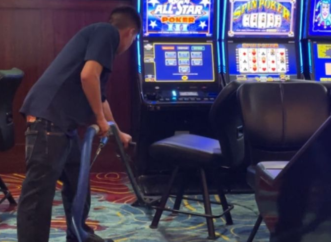 Person vacuuming beside a casino slot machine and chair