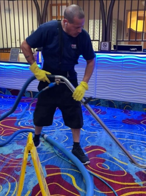 Man vacuuming a patterned carpet with a large hose in a colorful indoor venue