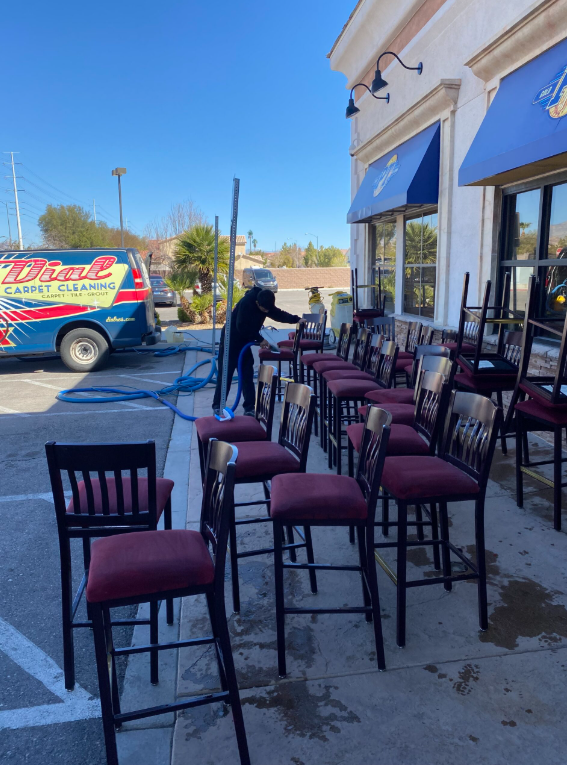 Outdoor cafe patio with empty burgundy chairs and tables beside a storefront, with a blue delivery van nearby