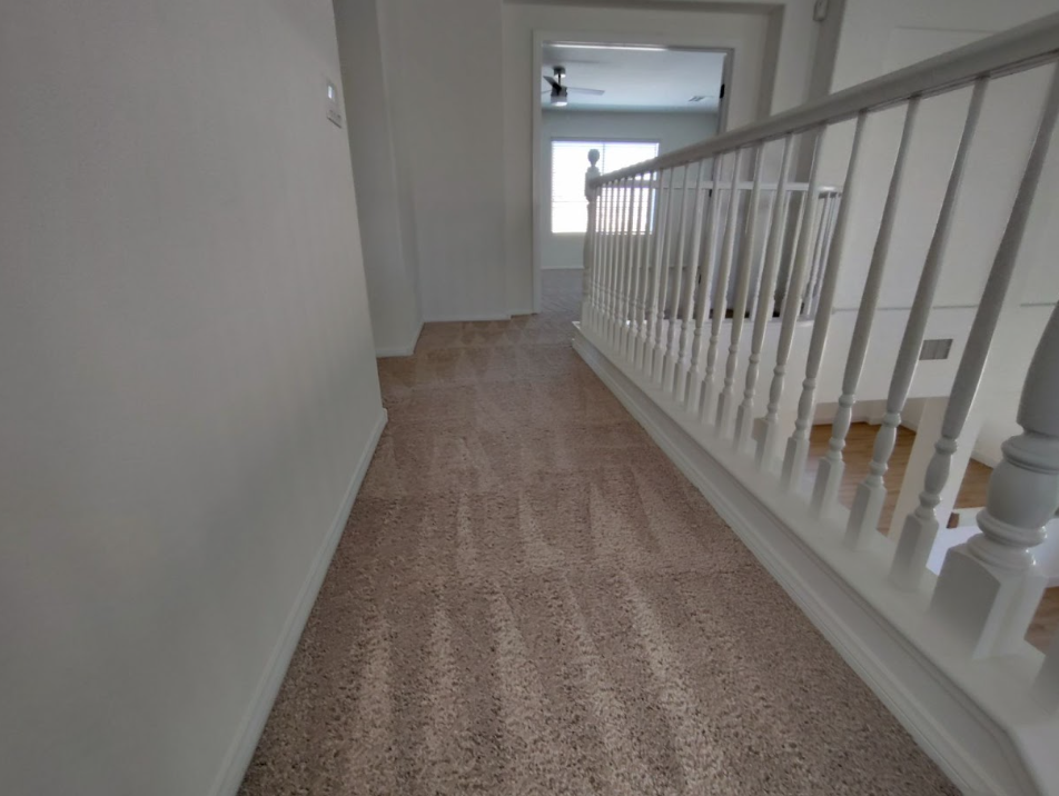 Carpeted hallway with white railing and walls, leading to a bright windowed landing.