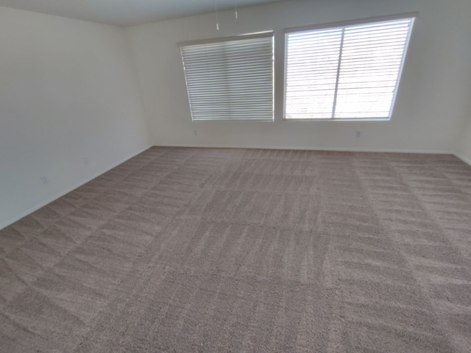 Empty carpeted room with white walls and two windows with blinds