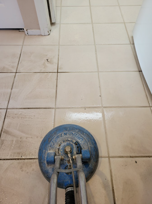 Blue floor cleaning machine on beige tiled floor in a hallway.