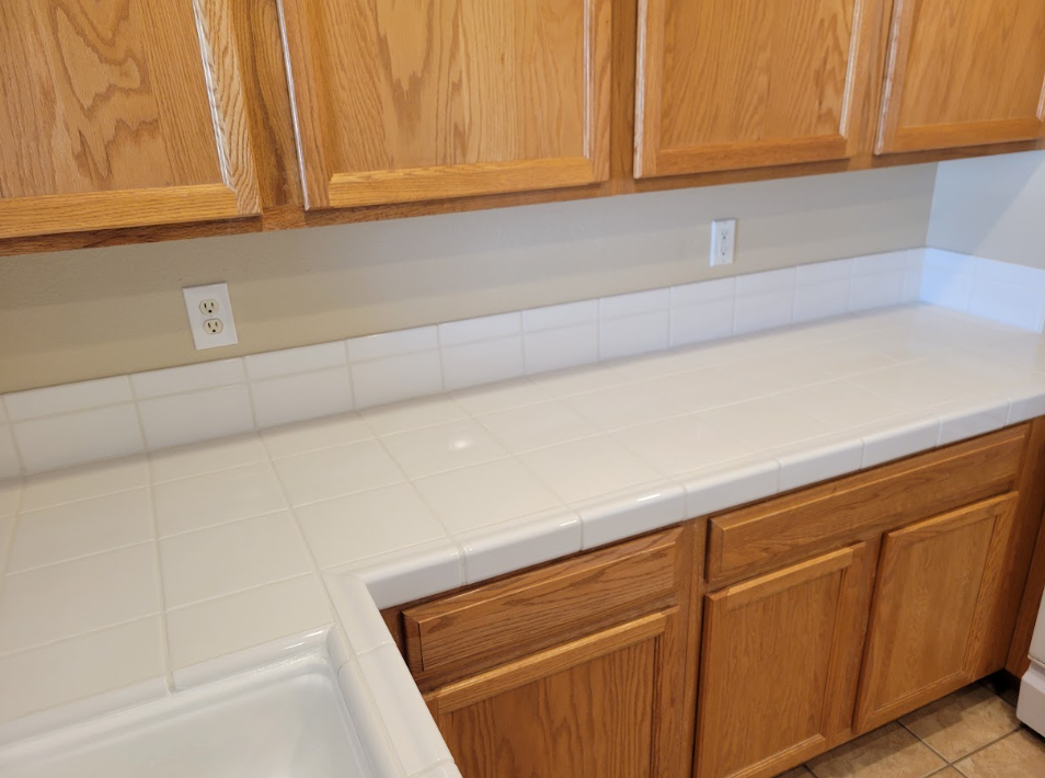 White tiled kitchen counter with wooden cabinets and backsplash outlets