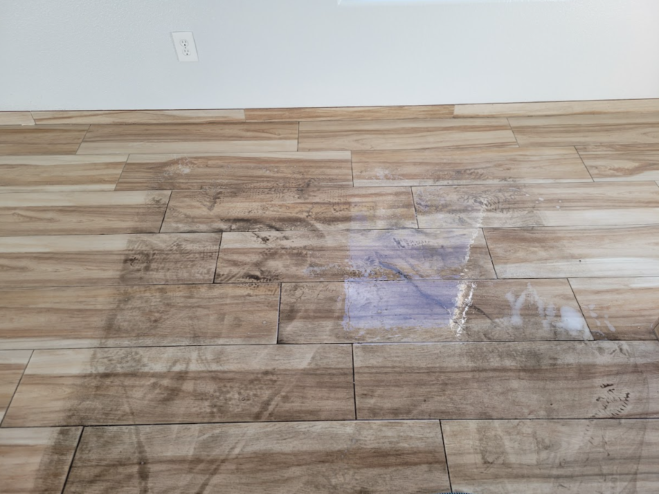 Scratched wood floor with a patch of white residue near the wall