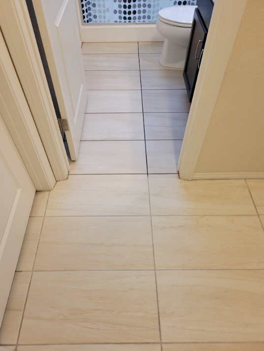 Narrow hallway with light tile floor leading to a bathroom with a toilet and blue mosaic shower wall.