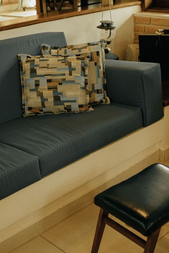 Modern sofa with patterned cushions beside a small stool in a warmly lit room.
